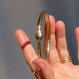 Gold bangle on a hand against a gray background