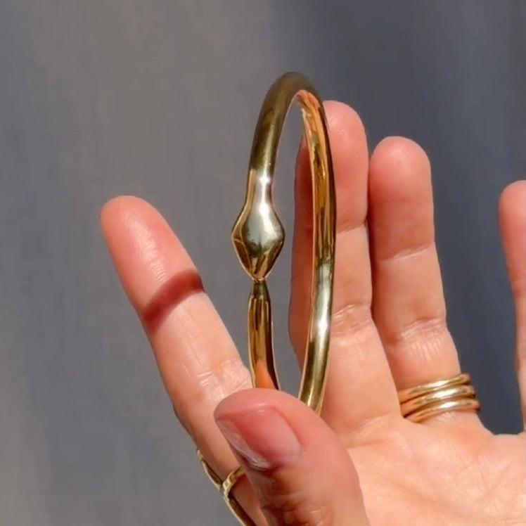 Gold bangle on a hand against a gray background